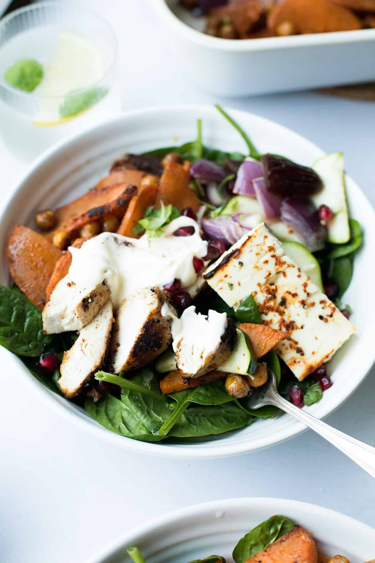 White bowl with fresh salad, baked feta cheese and roasted chicken.