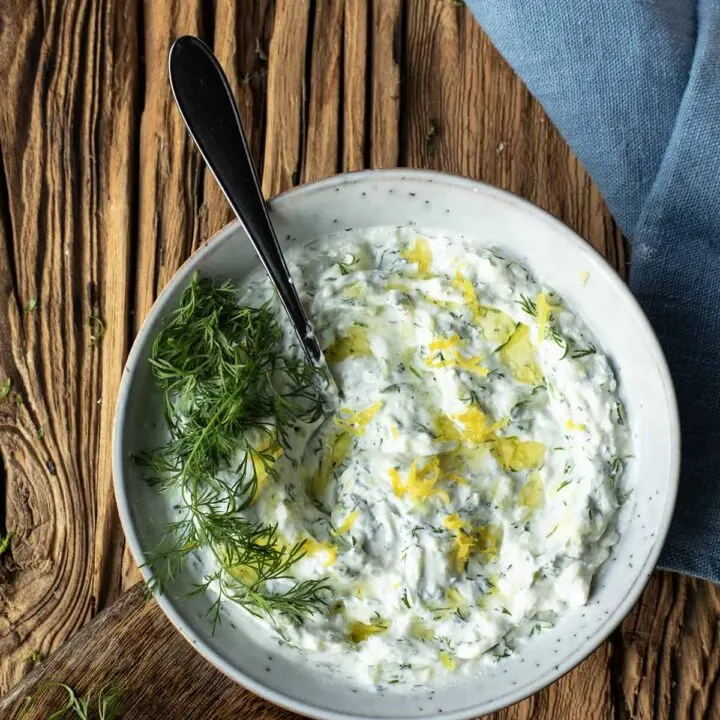 Close-up of tzatziki sauce with fresh dill and lemon zest on top.