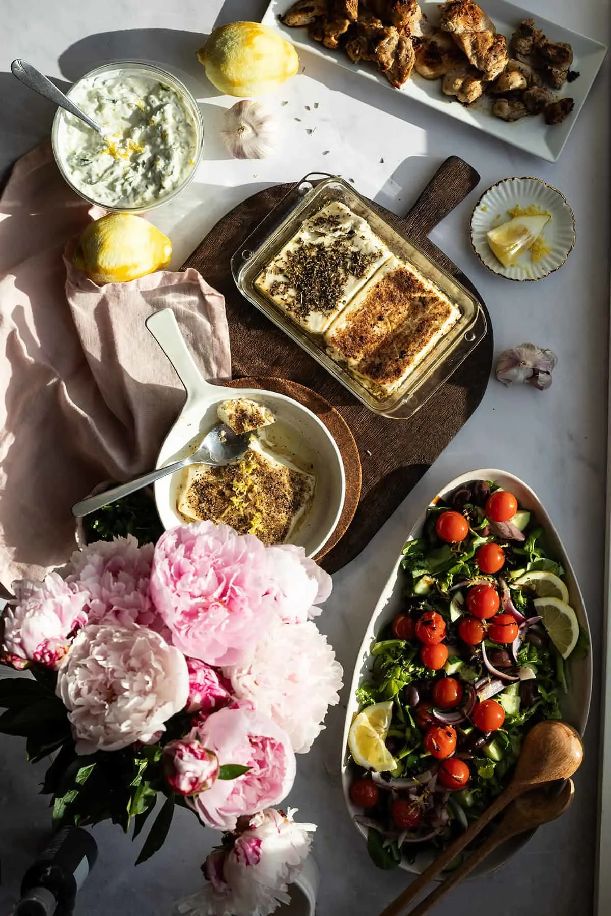 Closeup of a scene seen from above with salads, grilled chicken and baked feta cheese.
