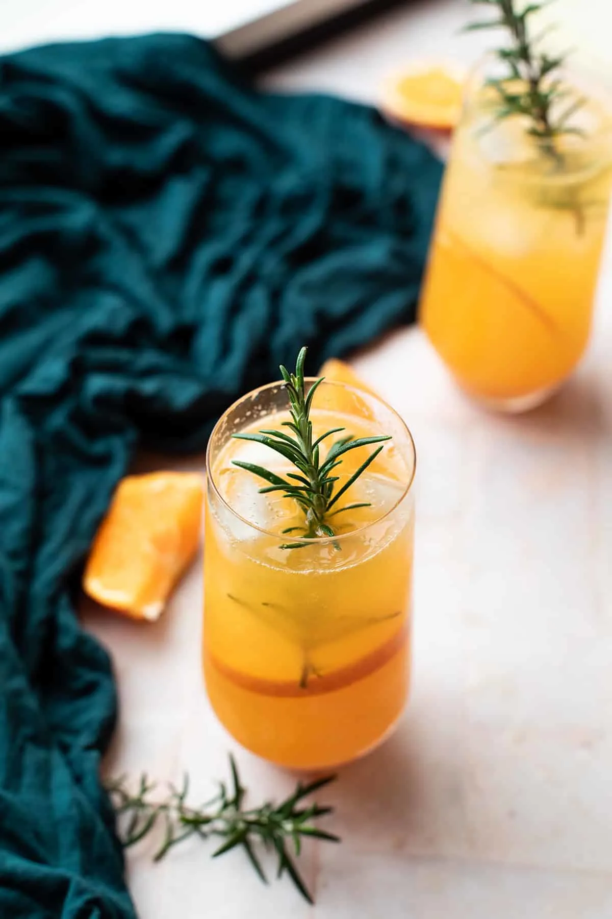 A stemless champagne flute with mandarin cocktail and a rosemary garnish.