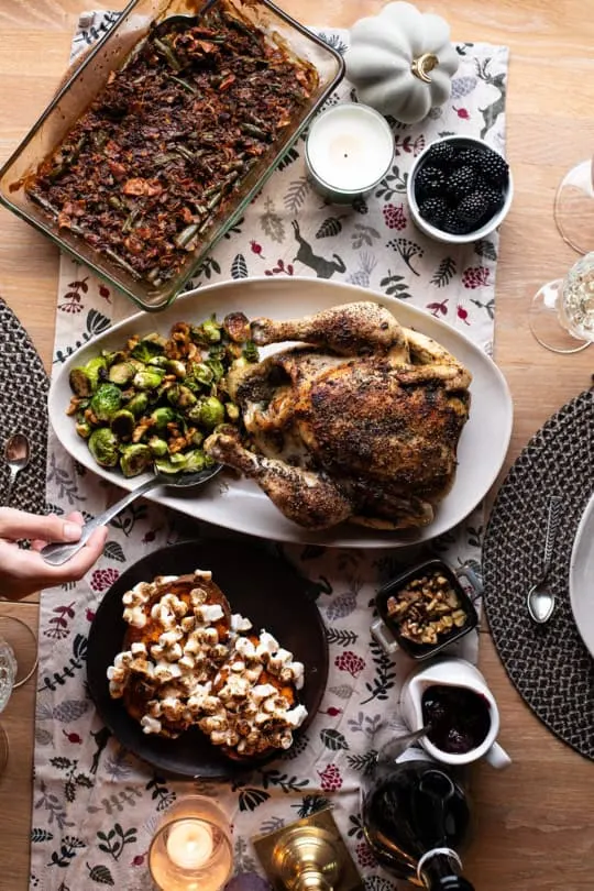 Thanksgiving dinnertable with whole roasted chicken, brussels sprouts, green bean casserole, sweet potato boats and a blackberry sauce.