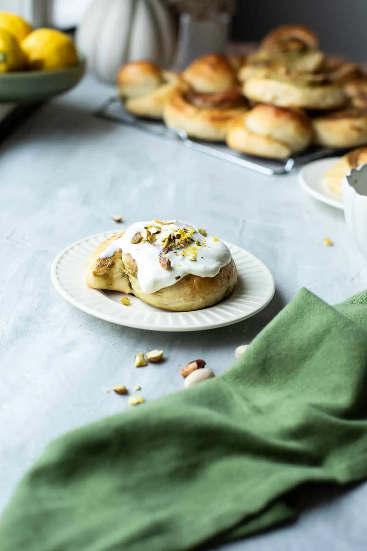 One pistachio roll on a white plate. More pistachio rolls in the background.