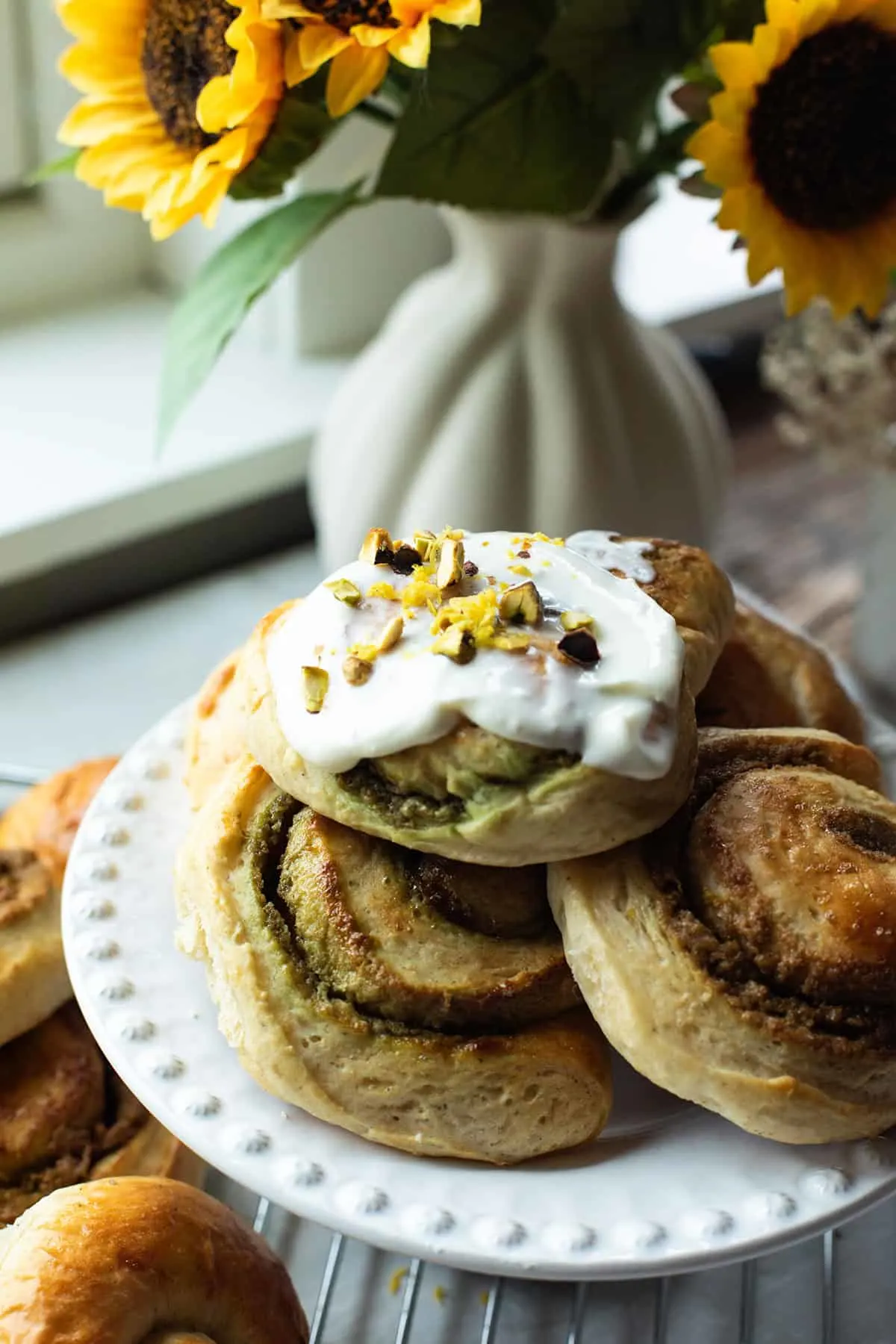 A cake tray with pistachio buns with cream cheese frosting.