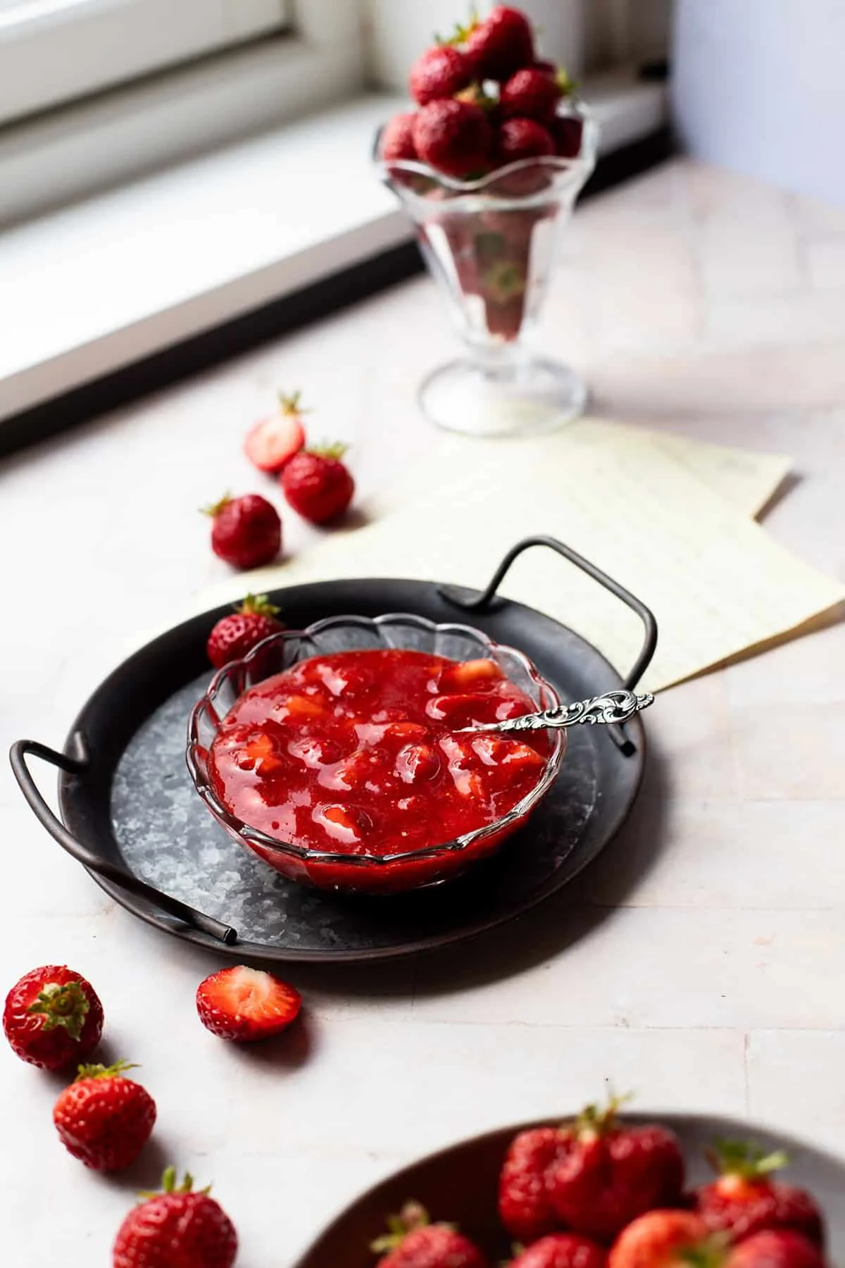 A glass bowl with strawberry freezer jam on a metal plate.