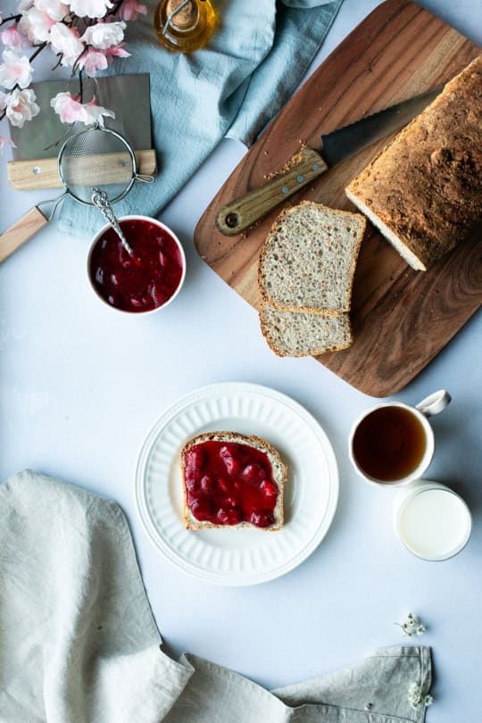 Bird's eye view of a white plate with a slice of bread with strawberry jam and the bread in one corner.