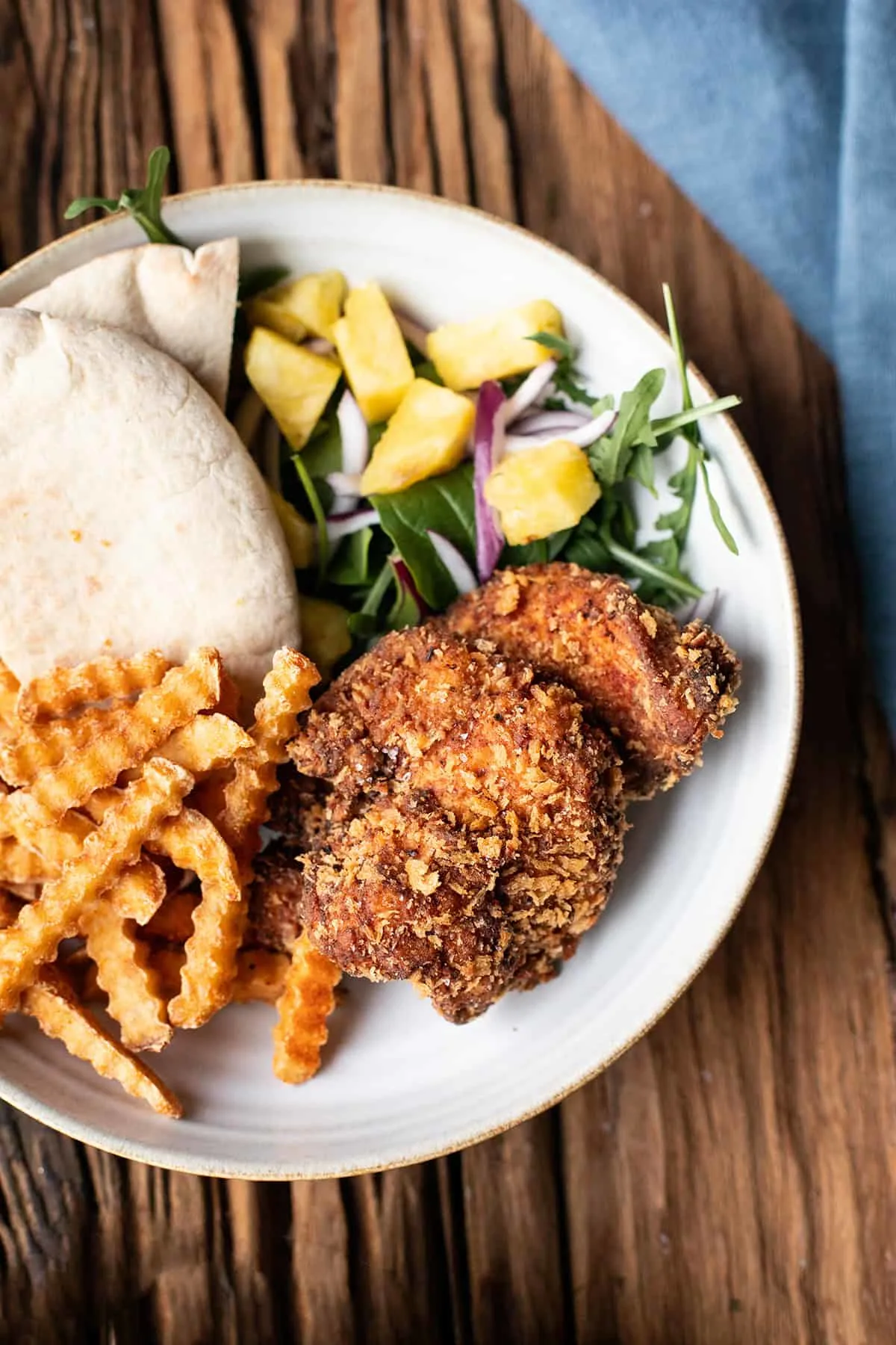 White plate with crispy cajun chicken, fries and a salad.
