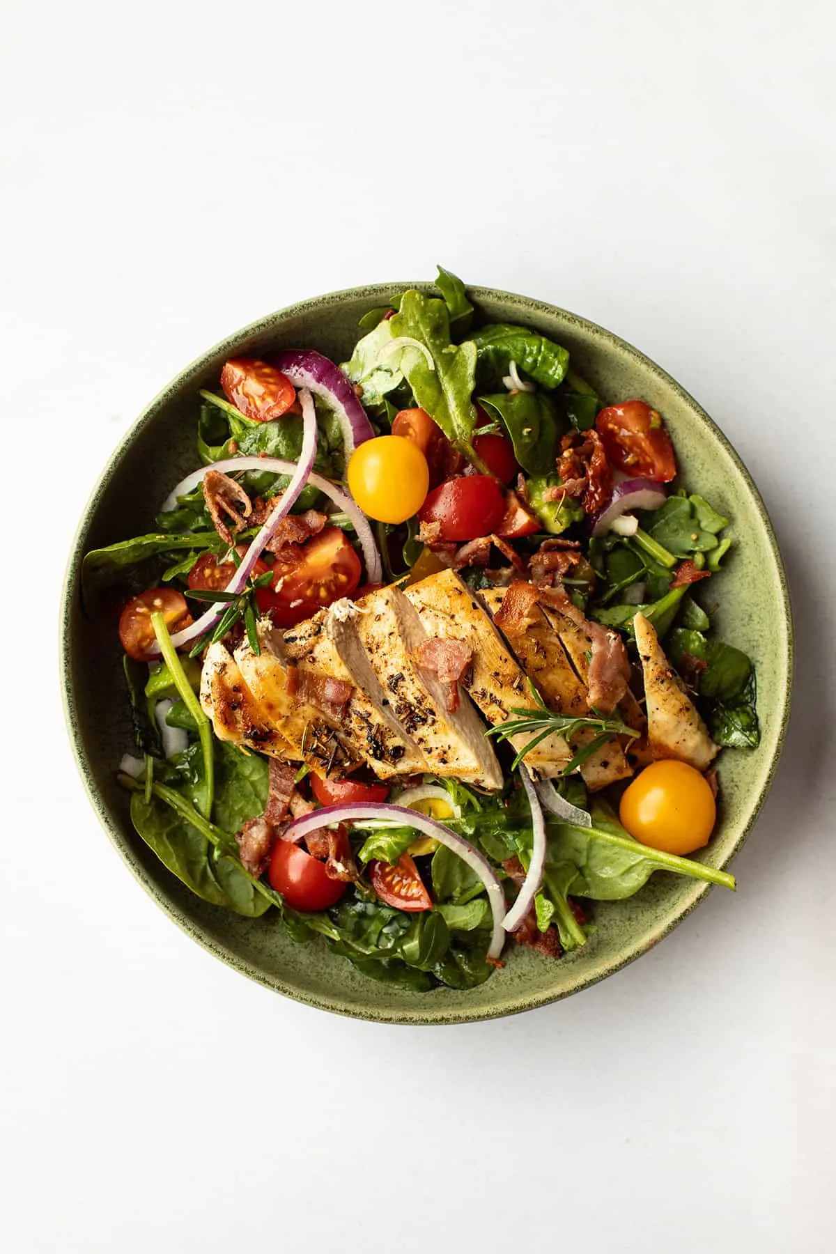 One sliced, grilled chicken breast on top of a bed of greens.