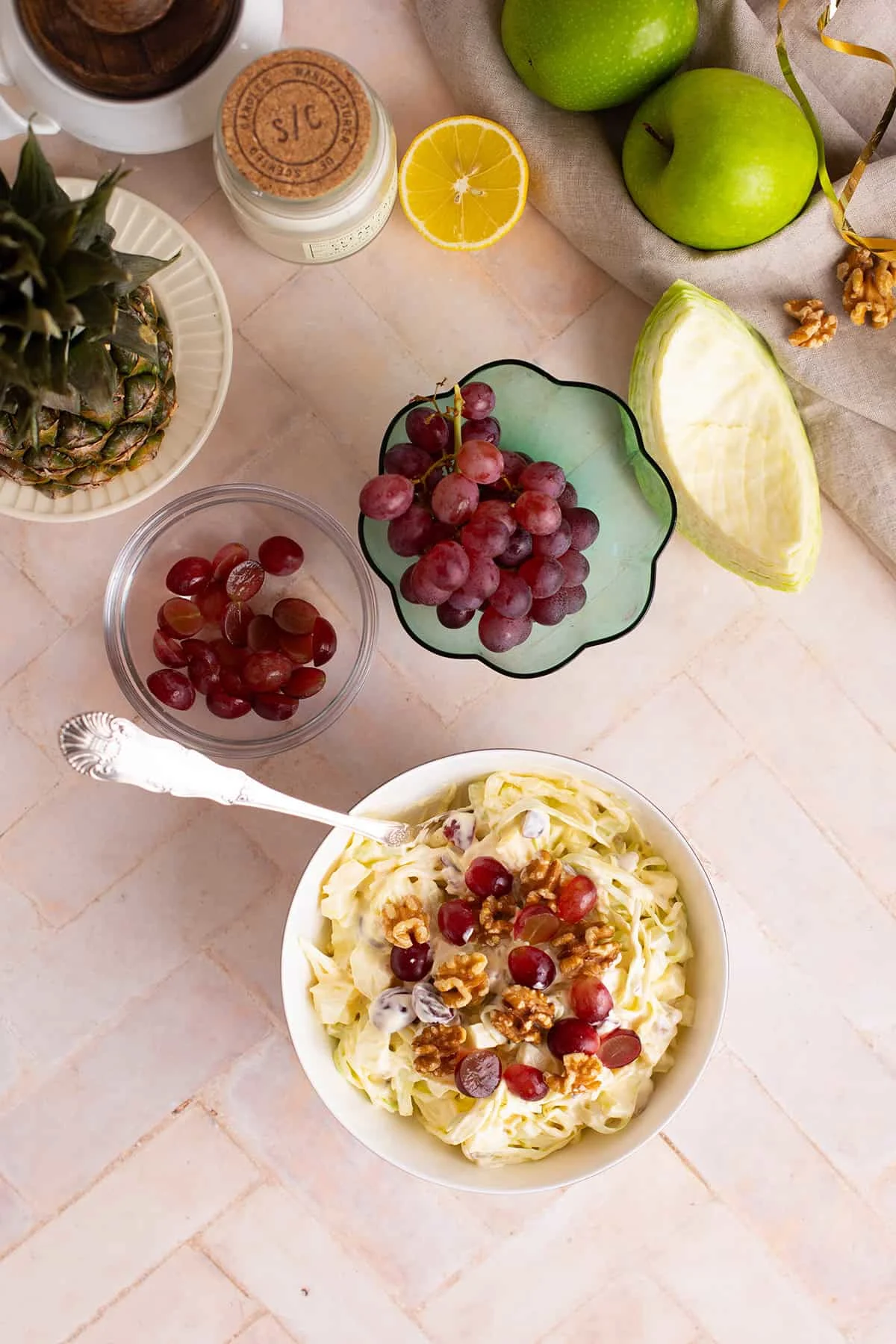 A serving bowl with Waldorf salad seen from above, bowls of grapes and other ingredients in the corner.