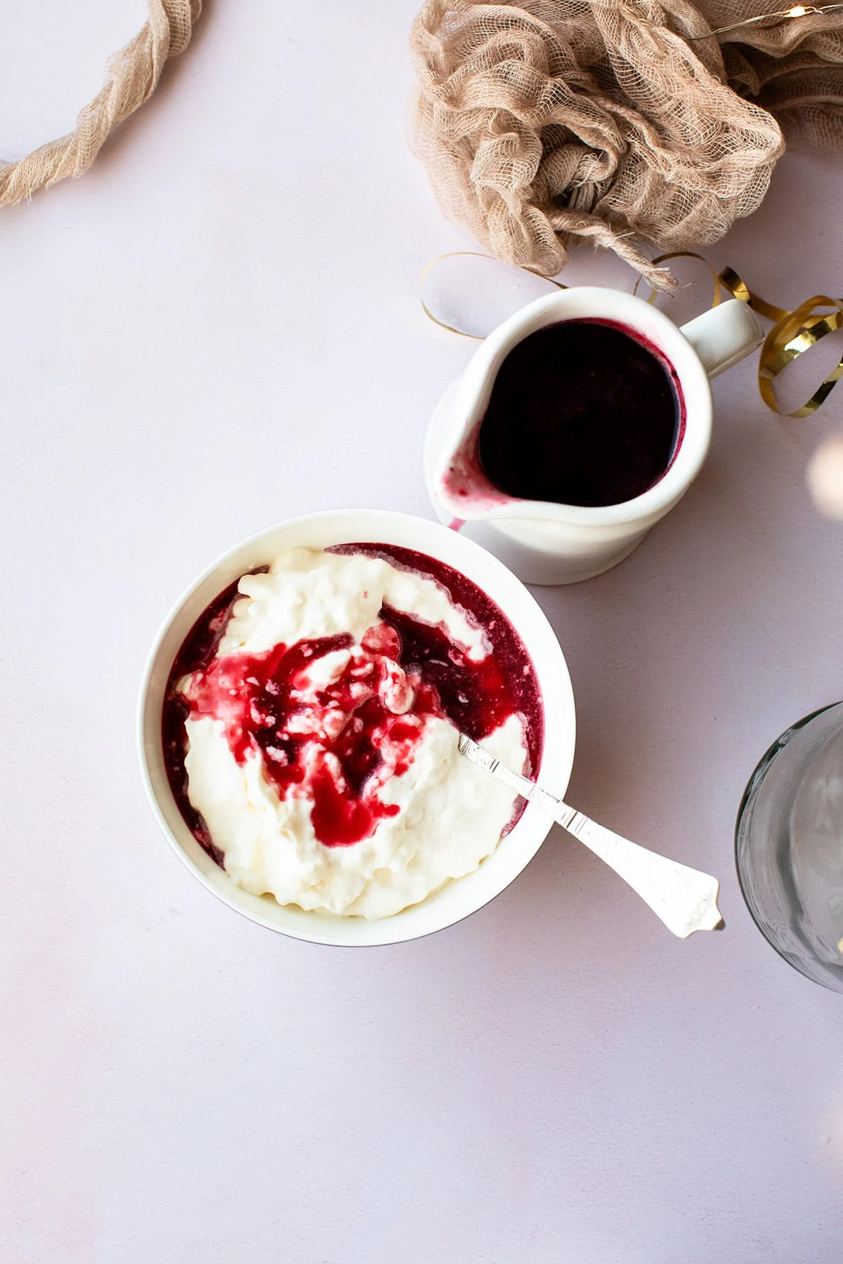 A small serving bowl of rice cream and a jug of berry sauce.