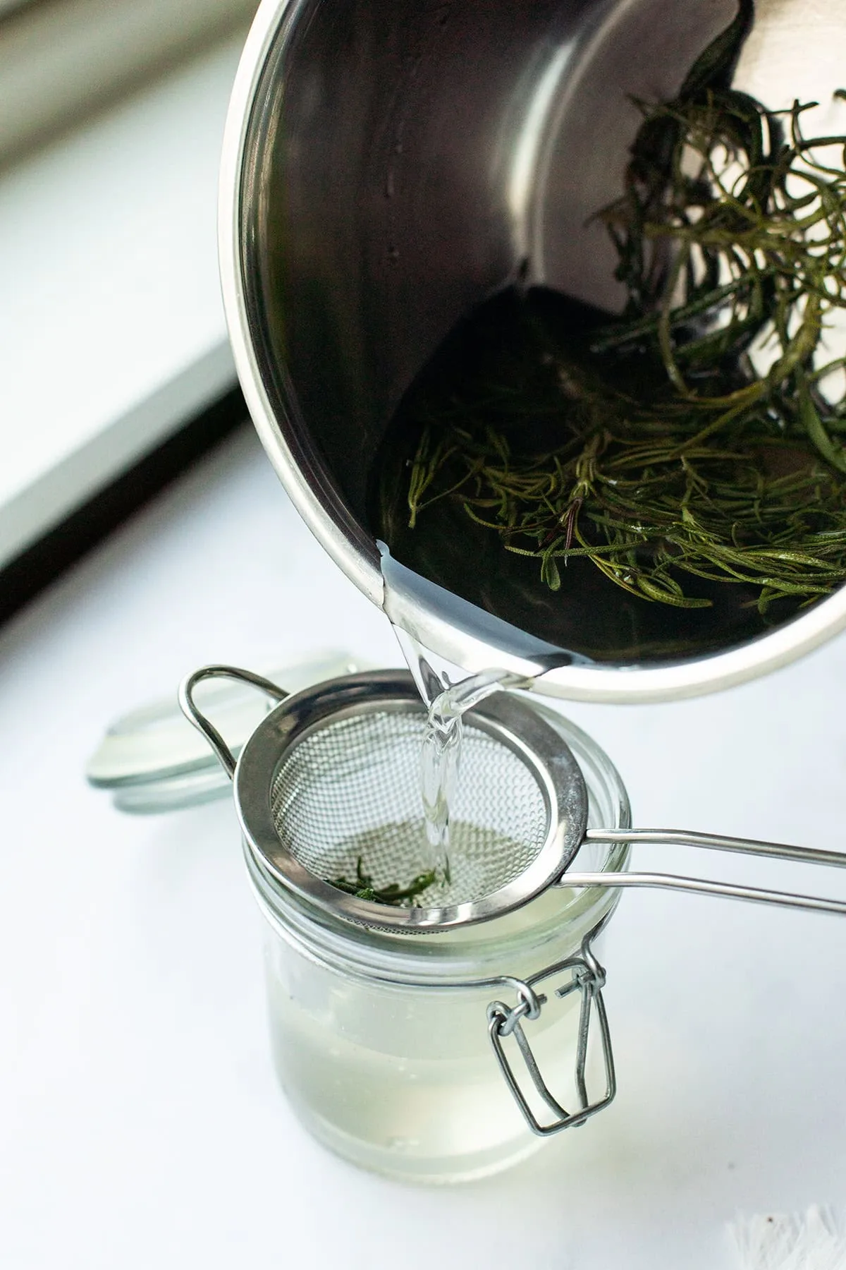 Pouring rosemary simple syrup in a jar.