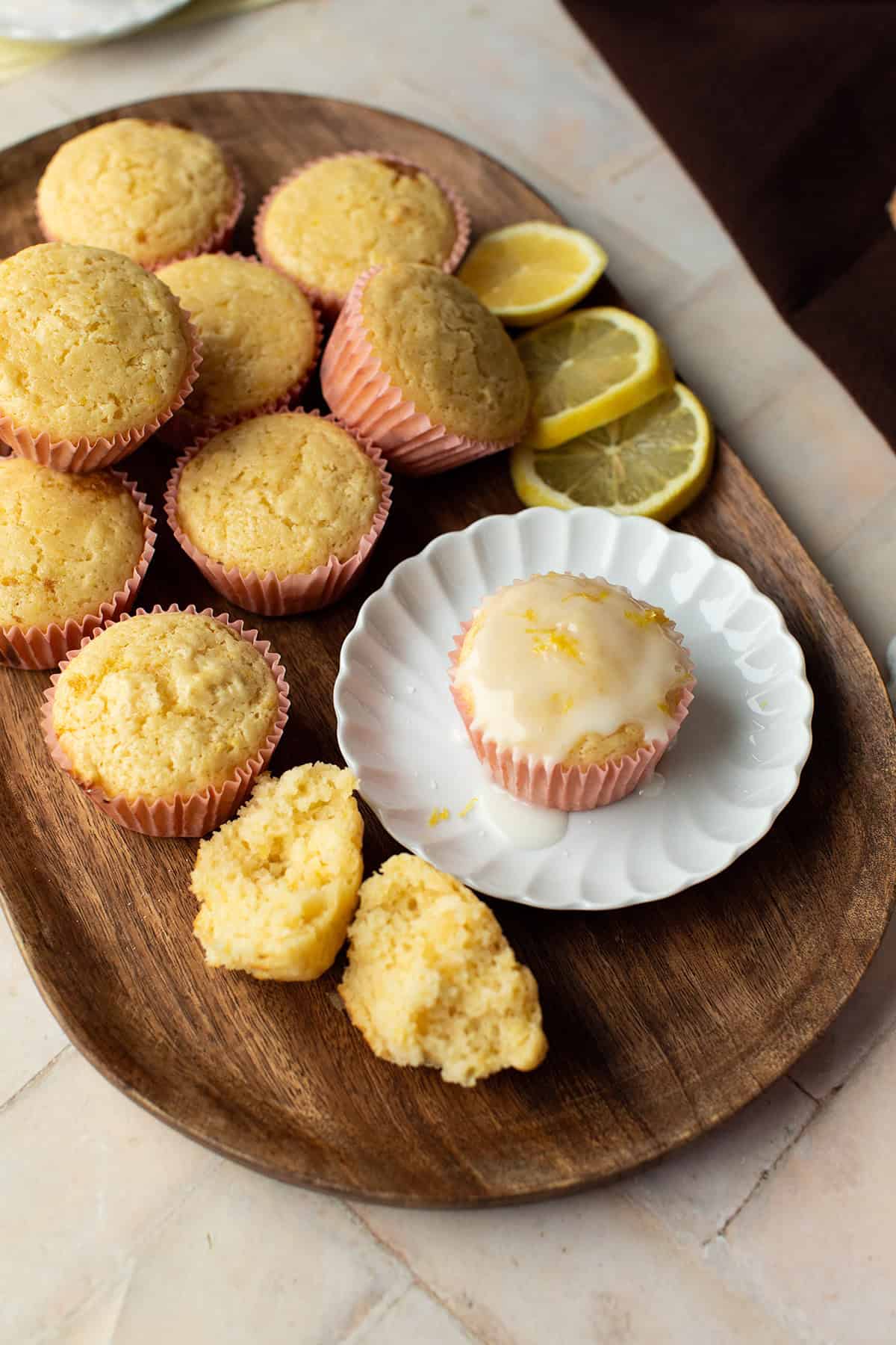 Lemon muffins on a wooden tray and one glazed on a small white plate.