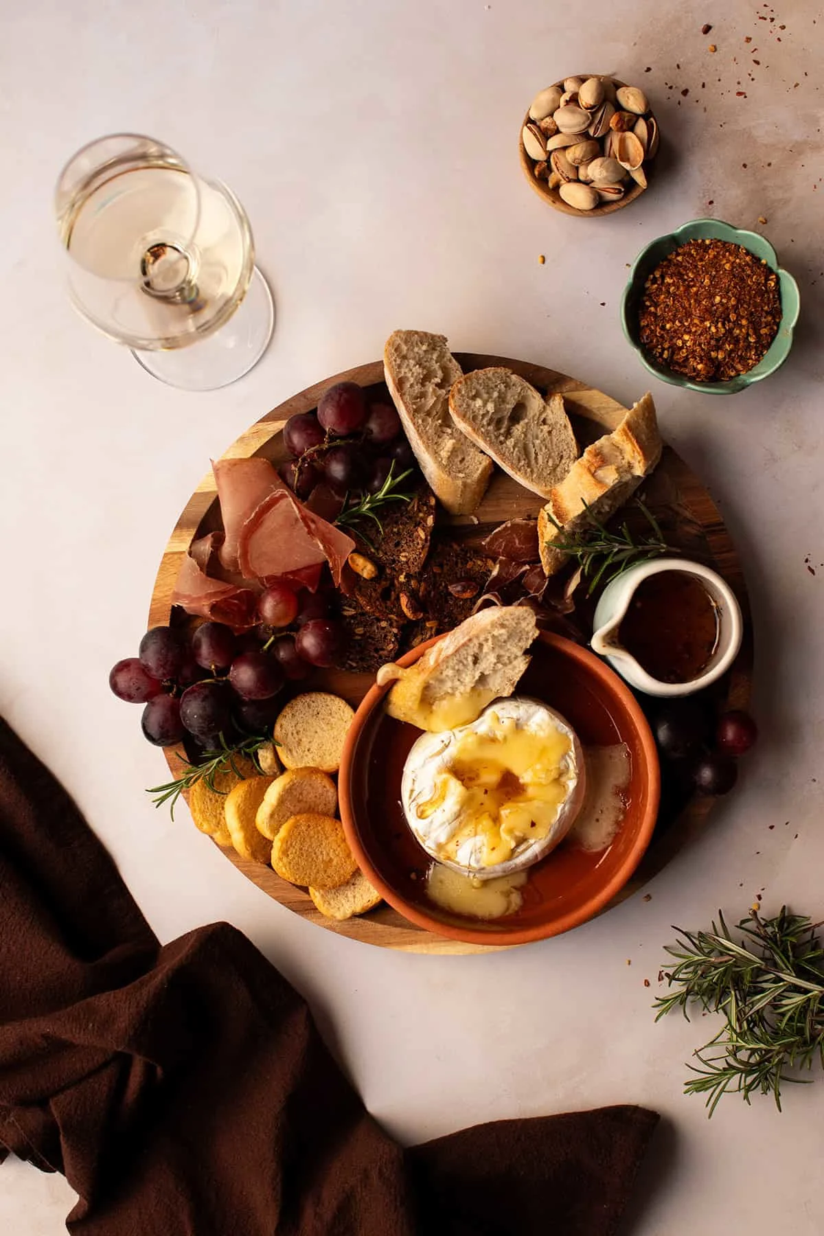 A wooden tray with hot honey brie, bread and grapes.