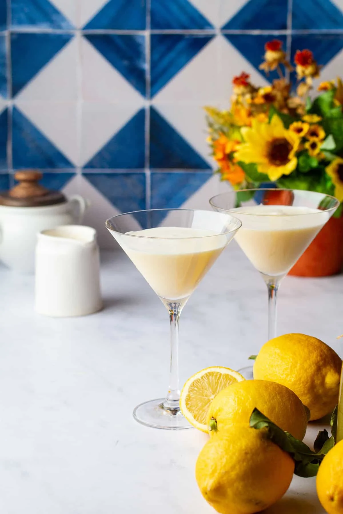 Two martini glasses with a creamy limoncello martini and lemons in the foreground.