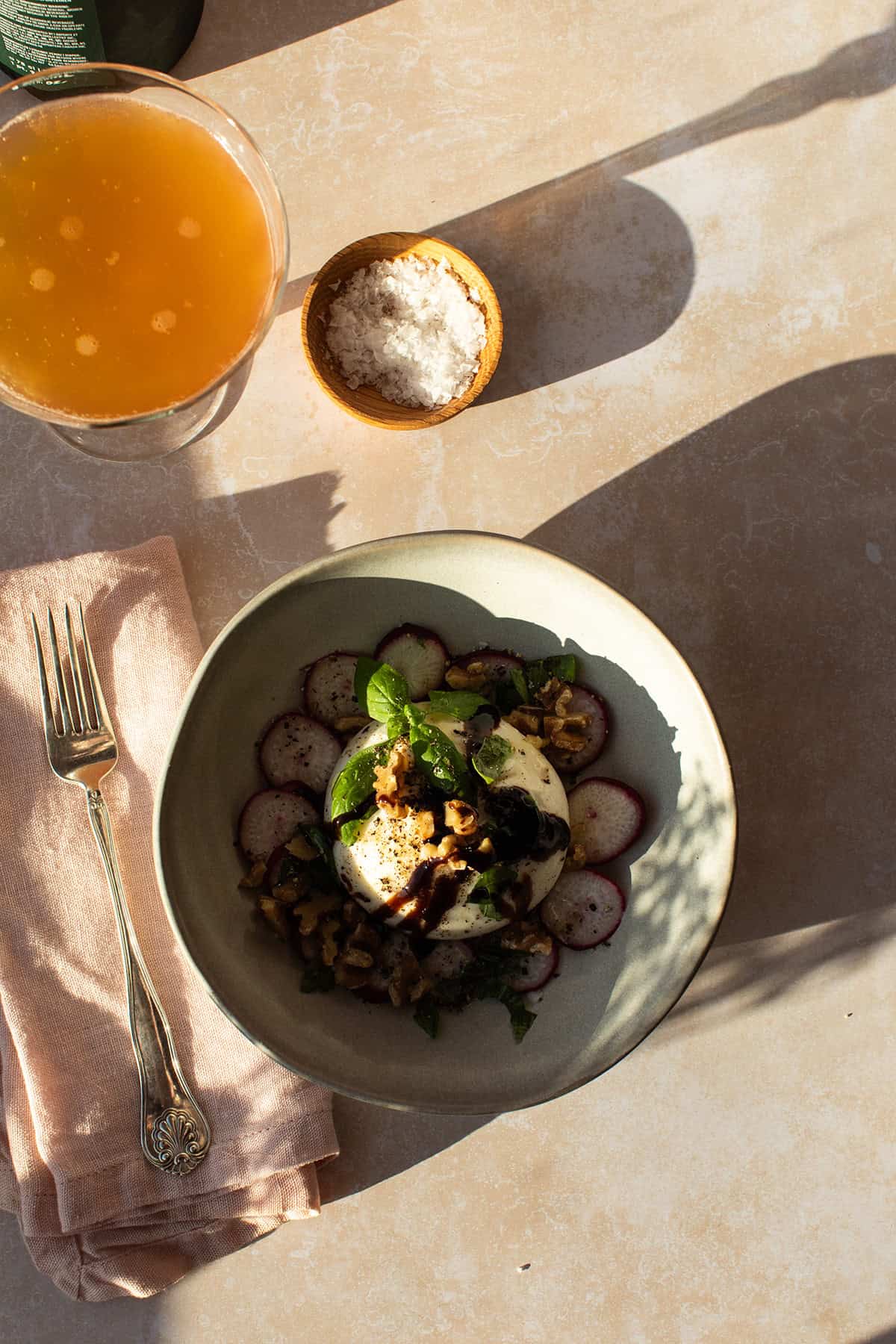 Ball of burrata surrounded by radishes in a serving bowl.