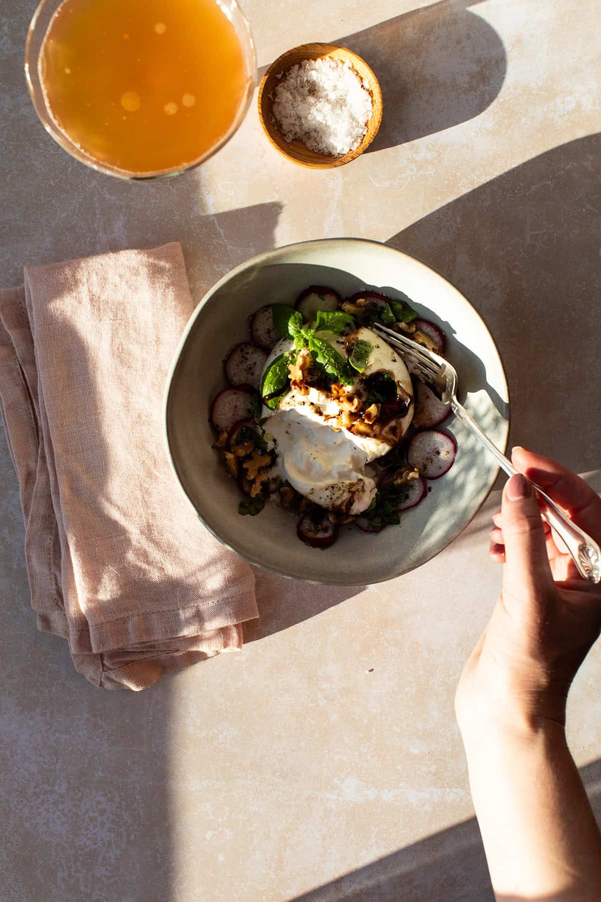 Hand holding a fork into the burrata appetizer.